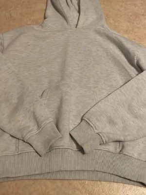 Ljusgrå basic hoodie - En enkel och stilren ljusgrå hoodie med huva och magficka. Tillverkad i mjukt sweatshirtmaterial med ribbade muddar vid ärmar och nederkant. Perfekt för en avslappnad och chill look.