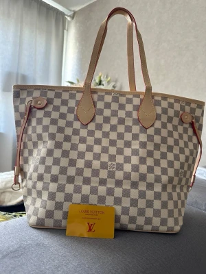 Louis Vuitton Neverfull bag - Säljer en snygg Neverfull väska från Louis vuitton Väskan är beige och vit med rutigt tryck, har ljusa läderhandtag med röda detaljer. Väldigt unik färg i beige som är svår att få tag på. Perfekt storlek för att få plats med allt du behöver. Ikonisk och trendig design!        Kontakta gärna över funderingar 