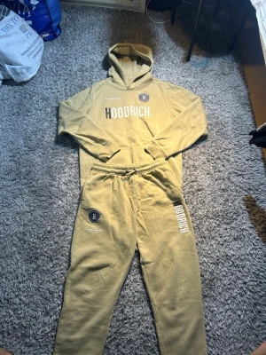 Beige HOODRICH loungewear set - Passar XS-S Säljer ett beige loungewear set från HOODRICH med matchande hoodie och byxor. Hoodien har stor logga framtill, huva och magficka. Byxorna har resår i midjan, tryckta loggor och avslappnad passform. Perfekt för chill dagar hemma.