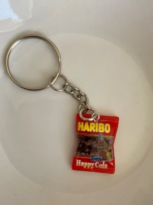 Nyckelring Haribo Happy Cola - Säljer en rolig nyckelring med en miniatyr av Haribo Happy Cola-godispåse. Ny.