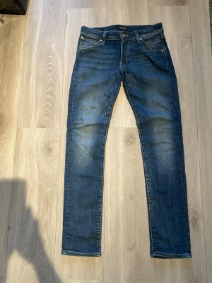 Jack&jones jeans - Snygga blå slim fit jeans med klassisk tvätt och fem fickor. Jeansen har en medelhög midja, dragkedjegylf och subtila slitningar framtill för en trendig look. Perfekta för dig som gillar en smal passform och tidlös stil.