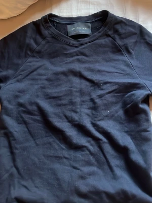 Svart sweatshirt från Dry Costume - En stilren svart sweatshirt från Dry Costume med rund halsringning och långa ärmar. Tröjan har en enkel design utan tryck eller mönster och är tillverkad i ett mjukt material som känns skönt mot huden. Perfekt för en avslappnad look. Står ingen storlek men är S