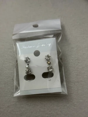Set med glittriga örhängen och pärla - Säljer ett set med fyra par örhängen i silverfärg. Två par har gnistrande stenar, ett par har en liten vit pärla och ett par har en liten guldfärgad detalj. Perfekta för att mixa och matcha till olika looks.
