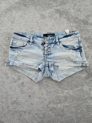 Low rise Tally Weijl shorts - Säljer ett par ljusblå jeansshorts från Tally Weijl med slitna detaljer, fransig kant och flera knappar framtill. Shortsen har klassiska fickor fram och bak. Perfekta till sommaren 