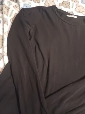 Svart långärmad topp i bomull - En basic svart långärmad topp med rund halsringning. Tillverkad i mjuk bomull, perfekt att styla lager på lager eller bära som den är. Enkel och stilren design som funkar till många outfits.