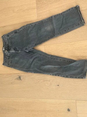 Grå raka jeans från Grunt - Säljer ett par grå jeans från Grunt med rak passform och klassisk femficksdesign. Jeansen har råa kanter vid bensluten för en trendig look och är tillverkade i denim. Perfekta för dig som gillar en avslappnad stil.