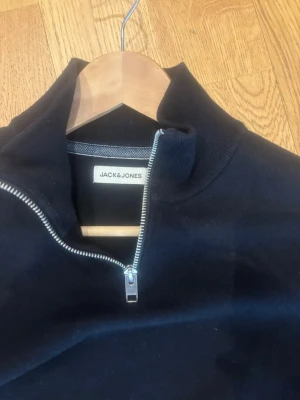 Svart halvzip-tröja Jack & Jones - Svart långärmad tröja från Jack & Jones med halv dragkedja och hög krage. Enkel och stilren design, perfekt för lager-på-lager. Tillverkad i mjukt material för en bekväm känsla.