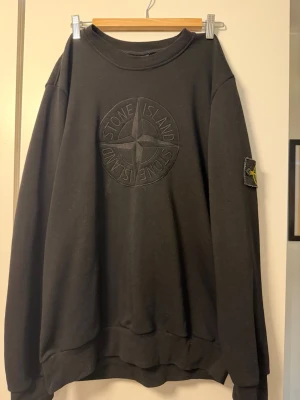 Svart sweatshirt från Stone Island - Svart sweatshirt från Stone Island med broderad logga på bröstet och klassisk patch på ärmen. Tröjan har en avslappnad passform och är tillverkad i mjuk bomull. Perfekt för en stilren och trendig look.