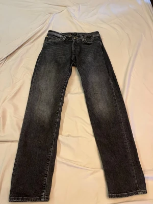 Jack and Jones jeans tapered - Snygga svarta jeans från Jack and Jones med raka ben och klassisk femficksdesign. Jeansen har en lätt tvättad look med subtila slitningar på låren. Perfekta för dig som gillar en stilren och tidlös vibe. 