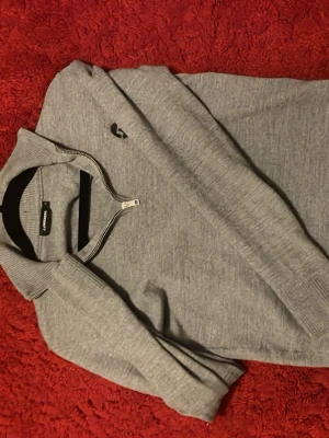 Grå halvzip tröja från J.Lindeberg - Snygg grå tröja från J.Lindeberg med halv dragkedja och ribbade muddar. Tröjan har en stilren look med diskret logga på bröstet och är tillverkad i mjukt material. Perfekt för lager-på-lager och passar till många outfits. Även perfekt för dig som vill ha en lite muskulös look då tröjan är lite tajtare på kroppen. Hör av dig om det förekommer någon fråga!