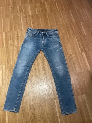 Blå slim fit jeans från Diesel - Snygga blå slim fit jeans från Diesel med slitna detaljer och klassisk femficksdesign. Jeansen har en ljus tvätt och är tillverkade i stretchigt denim för en bekväm passform. Perfekta för dig som gillar en trendig och avslappnad stil.