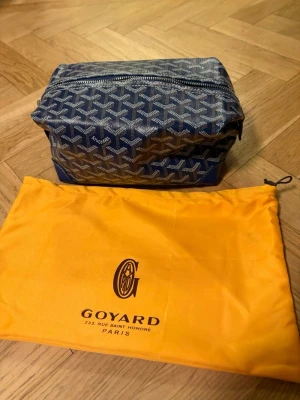 Blå necessär med mönster - Snygg blå necessär med klassiskt mönster i vitt och grått. Väskan har en rektangulär form, dragkedja upptill och kommer med en gul dustbag med. Perfekt för att organisera dina småsaker eller smink.
