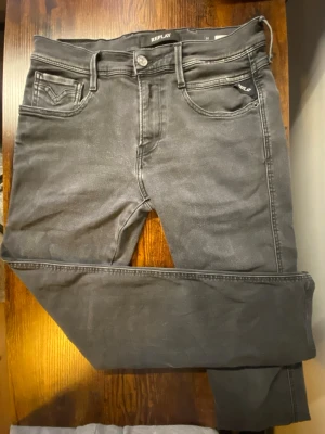 Svarta Replay Anbass  - Snygga svarta jeans från Replay med klassisk femficksdesign och diskreta slitningar. Jeansen har raka ben och tydliga sömmar, samt Replay-logga på fickan. Perfekta för en avslappnad och trendig look.