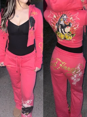 Ed Hardy tracksuit, size S - Säljer ett rosa loungewear-set från Ed Hardy med dragkedjetröja och byxa. Setet har stora tryck med pantermotiv, Ed Hardy-logga i guld och vita detaljer. Tröjan har huva och byxan har dragsko i midjan. Perfekt för en chill och snygg look.