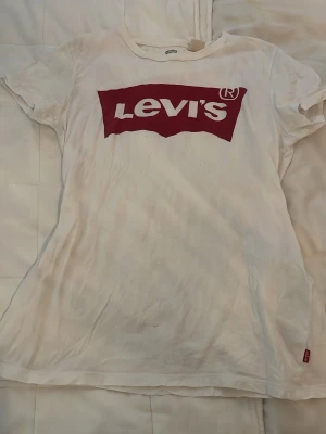 Vit Levi's t-shirt med röd logga - Vit t-shirt från Levi's i bomull med klassisk röd logga framtill. Modellen är kortärmad och har en normal passform. Perfekt för en avslappnad och stilren look.