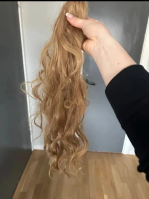 Mörkblond  lockig hårklämma - Säljer en lång, lockig hårförlängning med klämma i en naturlig  nyans. Perfekt för att snabbt fixa en fylligare frisyr med extra volym och längd. Klämman är diskret och enkel att fästa i håret. Materialet är syntetiskt och känns mjukt.