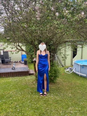 Blå långklänning - Säljer en elegant blå långklänning i glansigt material med smala axelband och djup v-ringning. Klänningen har en hög slits framtill och figurnära passform som framhäver siluetten. Perfekt för speciella tillfällen! Använd en gång.