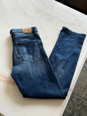 Blå raka jeans från Nudie Jeans - Säljer ett par klassiska blå jeans från Nudie Jeans med rak passform och snyggt slitna detaljer på låren. Jeansen har fem fickor, normal midja och är tillverkade i denim av bomull. Perfekta för en avslappnad och stilren look. Storlek står i bild 2