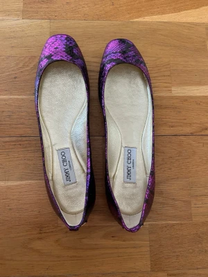 Lila ormmönstrade ballerinaskor Jimmy Choo - Snygga ballerinaskor från Jimmy Choo i lila och svart ormmönstrat material. Skorna är nästan oanvända och är i storlek 41.
