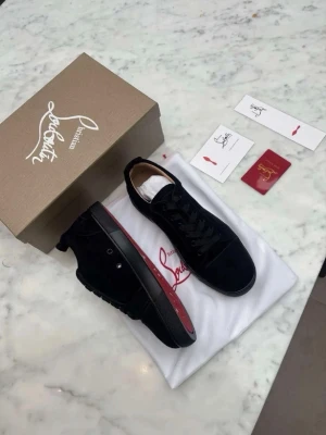 (Äkta) Christian Louboutin skor (Kvitto Finns) - Snygga svarta sneakers från Christian Louboutin med klassisk röd sula och diskret logga på sidan. Skorna har lågt skaft, svarta skosnören och är tillverkade i mocka och läder. Perfekta för dig som vill ha en exklusiv och stilren look.