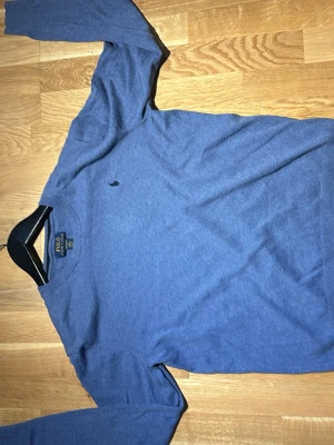 Blå långärmad tröja från Polo Ralph Lauren - Klassisk blå långärmad tröja från Polo Ralph Lauren med rund halsringning och diskret broderad logga på bröstet. Tröjan är i mjukt material och passar perfekt till jeans eller chinos.