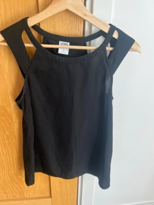 Snygg svart ärmlös topp från Vero Moda - Snygg svart ärmlös topp från Vero Moda med breda axelband och modern skärning. Perfekt till jeans eller kjol för en clean och stilren look. Tillverkad i mjukt material som känns skönt mot huden.