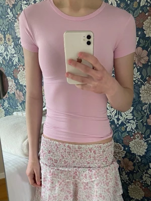 Ljusrosa tight t-shirt - Säljer en ljusrosa tight t-shirt med rund hals och korta ärmar. Toppen är enkel och stilren, perfekt att matcha med olika outfits. Materialet känns mjukt och stretchigt, vilket ger en bekväm passform.