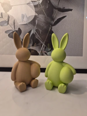Två söta påskkaniner - Säljer två söta kaninfigurer i beige och ljusgrönt. Figurerna är ribbade och har rundade former med stora öron och små svansar. Perfekta som dekoration i hemmet eller som present. Kaninerna är ca: 17cm höga.
