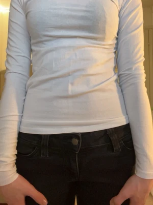 Vit långärmad topp i bomull - En enkel och stilren vit långärmad topp i bomull. Modellen är tight och har en klassisk rund halsringning. Perfekt att matcha med jeans eller kjol för en clean look.