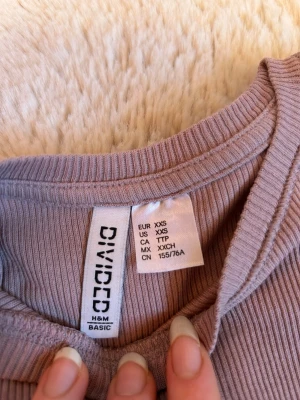 Ljuslila ribbad topp från H&M Divided - Säljer en ljuslila ribbad topp från H&M Divided. Toppen har rund halsringning och korta ärmar, i en slim passform som sitter snyggt på kroppen. Perfekt basplagg att styla med allt. Supermjuk och stretchig i materialet.
