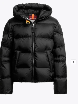 Svart pufferjacka från Parajumpers - Snygg svart pufferjacka från Parajumpers med huva och gul detalj vid halsen. Jackan har två stora framfickor, quiltad design och dragkedja framtill. Märkets logga syns på ärmen. Perfekt för kalla dagar och riktigt varm. — Tilly is a short hooded down jacket made of nylon taffeta, from the Hollywood family. The contemporary fit, bold look, and versatility make this down jacket perfect for everyday wear. Code: 25WMPGPUHY82PGC0541