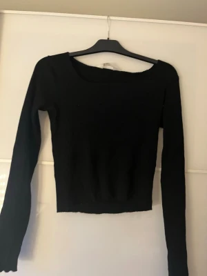 Svart ribbad croppad topp - En svart, croppad topp med lång ärm och ribbad struktur. Toppen har en bred, rundad urringning och sitter tight mot kroppen. Perfekt att styla med höga jeans eller kjol för en clean look. Från Hm