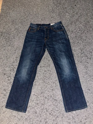 Hugo boss jeans - Säljer ett par mörkblå jeans från Hugo Boss med raka ben och klassisk femficksmodell. Jeansen har snygga slitningar framtill och kontrastsömmar. Tillverkade i kraftig denim med läderpatch bak i midjan. Perfekta för en avslappnad och trendig look.
