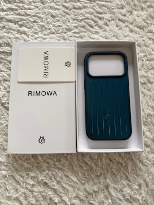Blått mobilskal från Rimowa - Snyggt blått mobilskal från Rimowa med klassisk räfflad design och robust känsla. Skalet är tillverkat i hårdplast och har en stilren, modern look med öppning för kameran. Perfekt för dig som vill ha ett exklusivt och tåligt skydd till din mobil. 
