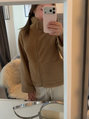 Brun teddyjacka från H&M - Mysig teddyjacka i brun från H&M med hög krage, dragkedja framtill och två stora fickor. Jackan har en avslappnad passform och är tillverkad i mjukt, fluffigt material som håller dig varm. Perfekt för att skapa en chill och trendig look. Köptes från plick för 500 kr, har typ aldrig använts sen dess 