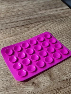 Pop it fidget och dubbelhäftande tejp - Praktisk mobilhållare i cerise silikon med sugproppar för att enkelt fästa mobilen på olika ytor. Rektangulär form och självhäftande baksida med 3M-tejp gör den smidig att använda i bilen, på skrivbordet eller andra släta ytor.