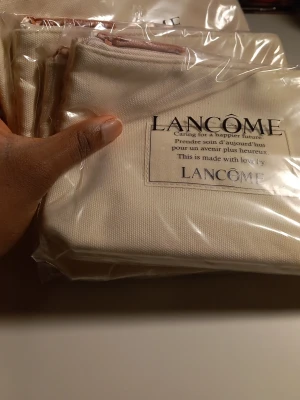 Beige necessärer från Lancôme - Säljer fyra beige necessärer från Lancôme i canvasmaterial med dragkedja upptill. Necessärerna har tryckt text på framsidan och är perfekt för att förvara smink eller småprylar. Enkel och stilren design med praktisk storlek.