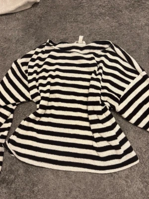 Svartvit randig stickad tröja - Säljer en stickad tröja med svarta och vita horisontella ränder. Tröjan har rund halsringning och långa ärmar. Materialet är mjukt och stretchigt, perfekt för en avslappnad look. Passar till jeans eller kjol för en enkel men snygg outfit.