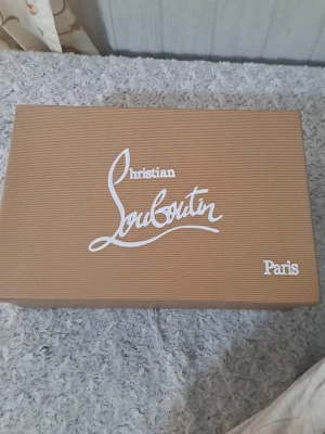 Christian Louboutin skokartong - Säljer en exklusiv skokartong från Christian Louboutin Paris. Kartongen är brun med vit logga och innehåller dustbags och äkthetskort. Perfekt för dig som vill ha en snygg förvaring till dina Louboutin-skor.