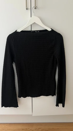 Svart ribbad långärmad topp - Säljer en svart långärmad topp med ribbad struktur och vågig kant. Toppen har en enkel, stilren design och är perfekt att matcha med både jeans och kjol. Materialet känns mjukt och stretchigt för en bekväm passform.