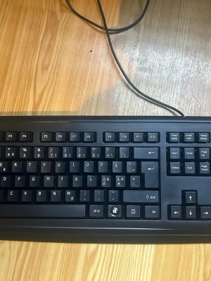 Svart trådbundet tangentbord - Klassiskt svart tangentbord med nordisk layout och USB-kabel. Tangenterna har tydliga vita tecken och tangentbordet har fullstor design med numerisk del. Perfekt för både gaming och skrivarbete vid datorn.