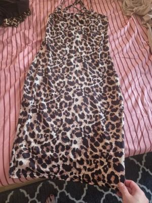 Leopardmönstrat nattlinne med smala band - Snyggt klänning med leopardmönster i beige, brunt och svart. Modellen har smala axelband och en djup rygg med dekorativa banddetaljer. Materialet känns mjukt och följsamt, perfekt för chillkvällar hemma.