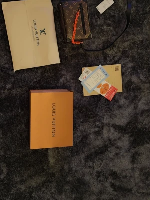 Louis Vuitton Monogram handväska - Snygg handväska från Louis Vuitton i klassiskt brunt monogrammönster med svarta detaljer och en cool orange kedja. Väskan har justerbar axelrem och levereras med förpackning och dustbag. Perfekt accessoar för dig som vill sticka ut.