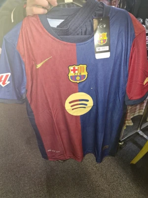 Barcelona matchtröja Nike röd/blå plus shorts - Snygg FC Barcelona matchtröja från Nike i klassiska rödblå färger. Tröjan har klubbmärke, Nike-logga och Spotify som sponsortryck på bröstet. Tillverkad i lätt och ventilerande material med Dri-FIT-teknologi. Perfekt för fotbollsträning eller att bära till vardags.