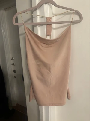 Beige linnetopp med strassdetalj - Trendig beige linnetopp med tunna axelband och snygg draperad urringning. Toppen har en unik strassdetalj i ryggen som ger extra bling. Perfekt för dig som gillar minimalistisk men ändå iögonfallande stil. Materialet känns mjukt och har en lätt glans.