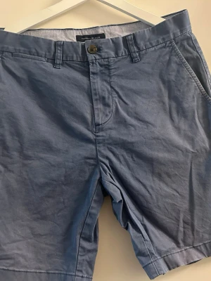 Blåa shorts från Tommy Hilfiger storlek 32 - Snygga blåa shorts från Tommy Hilfiger med klassisk passform. De har bälteshällor, knappgylf och två sidofickor fram samt två bakfickor med knapp. Perfekta för sommardagar och har en stilren look. Storlek 32