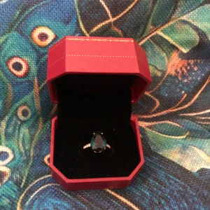 Guldfärgad ring med blå sten - Snygg guldfärgad ring med en stor droppformad blå sten i centrum. På sidorna av ringen sitter små klara stenar som ger extra bling. Perfekt statement-piece för dig som vill sticka ut med något unikt och färgstarkt. Diamanter / ädelstenar är äkta och ringen är gjord av 14 g guld. Den är köpt från Tianyo Gems.