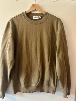 Olivgrön sweatshirt från Weekday - En enkel olivgrön sweatshirt från Weekday med rund halsringning och ribbade muddar vid ärmslut och nederkant. Tillverkad i mjuk bomull och har en relaxed passform som passar perfekt till jeans eller mjukisbyxor.