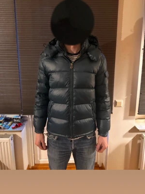 Mörkgrön dunjacka från Moncler - Snygg mörkgrön dunjacka från Moncler med huva och dragkedja framtill. Modellen är 187cm och väger 80kg