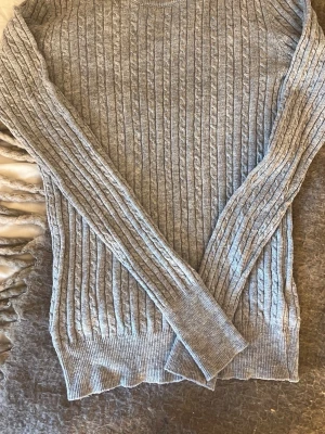 Grå kabelstickad tröja Gina Tricot - Säljer en grå kabelstickad tröja från Gina Tricot. Tröjan har rund halsringning, långa ärmar och ribbade muddar vid ärmslut och nederkant. Perfekt för lager på lager och enkel att matcha med jeans eller kjol.